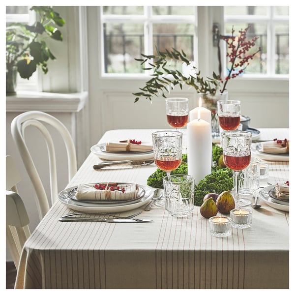 Dining table set for meal with white chairs, glasses, plates, and candles.