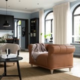Brown leather VISKAFORS armchair, arched windows, black coffee table, modern kitchen.