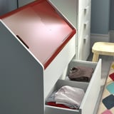 Open white VITBJÖRN storage unit with gray drawers, one holding folded gray and red clothes, against blue wall.