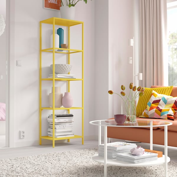 Yellow VITTSJÖ shelf with books, vases, glass shelves, next to sofa.