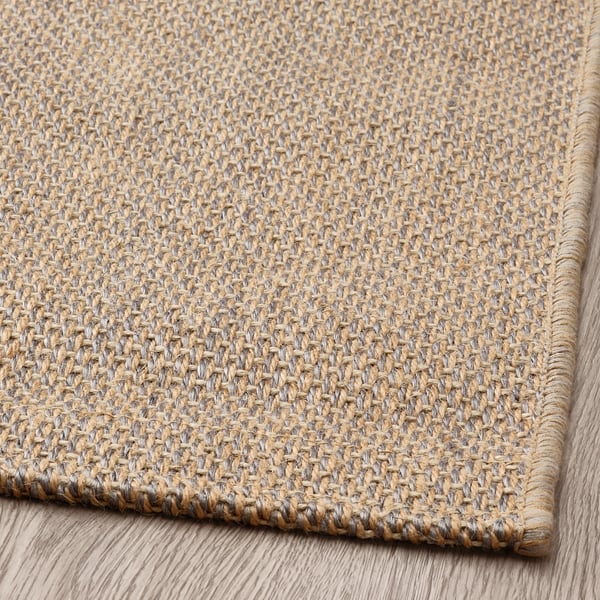 Natural fiber rug, tightly woven with jute and sisal, laid on wooden floor. Durable, textured surface, anti-slip backing.