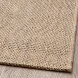 Natural fiber rug, tightly woven with jute and sisal, laid on wooden floor. Durable, textured surface, anti-slip backing.