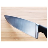 A sharp, stainless steel chefs knife with a black handle rests on a wooden cutting board, showcasing its sleek design and high-quality craftsmanship.