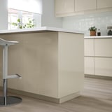 Modern kitchen with high-gloss beige VOXTORP cabinets, sleek handles, and a white countertop. Tall units dominate, with a bar stool to the side.