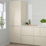 Modern kitchen with large cream-colored VOXTORP cabinets. High-gloss finish. Tall cabinets taller than window. Plants on counter.