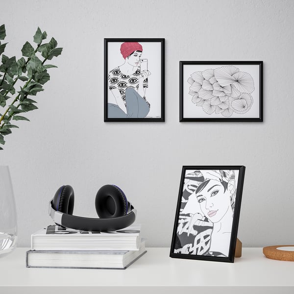 Desk with headset, books, framed art. Wall has two pictures, one on desk. Black frames: floral, woman.