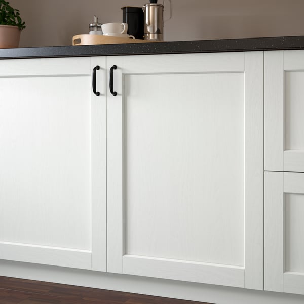 Kitchen cabinets with white, wood-like foil. Dark handles and countertop with coffee items.