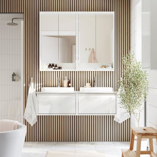 Modern bathroom with ÄNGSJÖN white vanity, double sinks, striped wall, and mirror; large plant beside it.