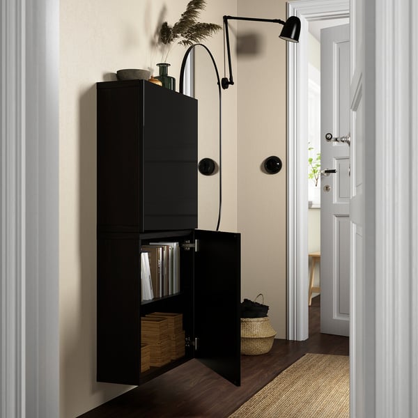 Black wall-mounted cabinet, partially open, revealing organised interior with files and boxes. Mounted lamp above.