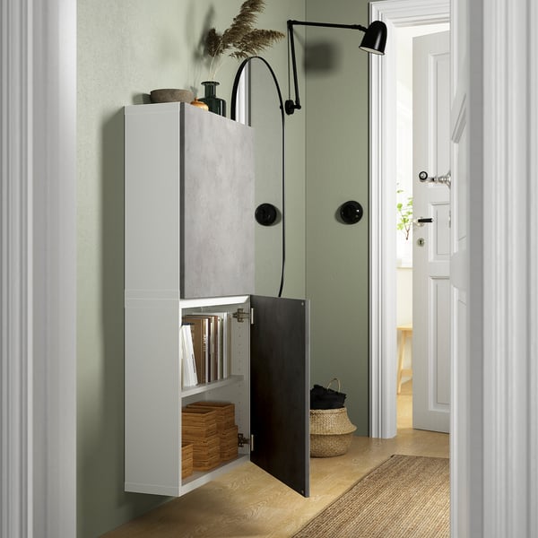 Wall-mounted BESTÅ cabinet with books and decor. One door open, concrete effect on other, black lamp above.