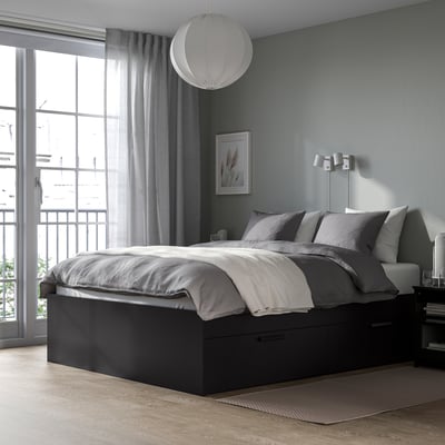 Modern black BRIMNES bed with drawers, grey pillows, and curtained window. Large, fits rooms well.