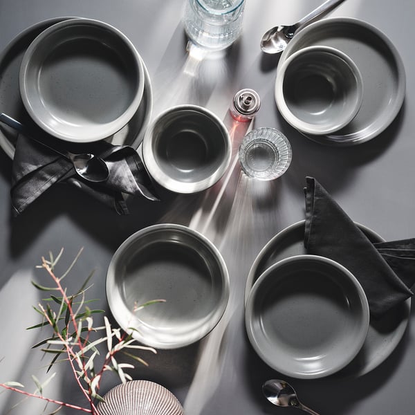 Grey stoneware bowls & plates with speckles, rustic style, medium size, table setting with napkins, bottle, shaker, spoons, plant.