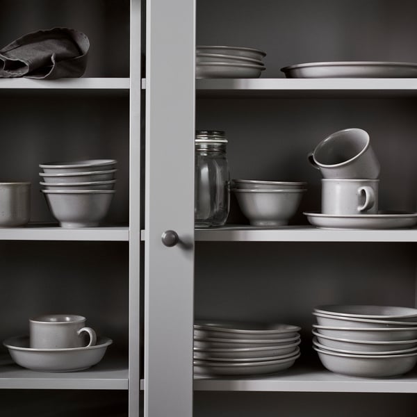 Open pantry showing DAGGASTER grey stoneware dishes. Includes mugs, plates, bowls, and jars neatly stacked. Simple, rustic design with earthy tones.