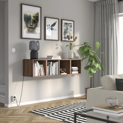Modern living room with EKET shelf, books, vase, lamp, prints, plant, armchair, and striped rug.