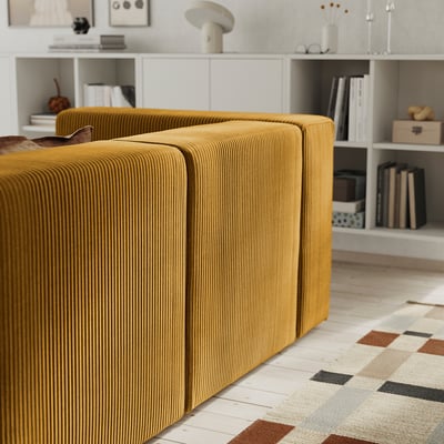 Mustard modular sofa with plush cushions sits on a patterned rug, showcasing its comfortable and inviting design.
