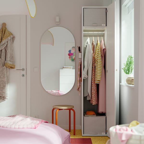 A childs bedroom with a pink wardrobe open, revealing colourful clothes; a mirror and stool in front.