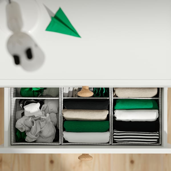 Organised drawer with labelled compartments. Clothes neatly stacked in sections. Green paper plane decor on top.