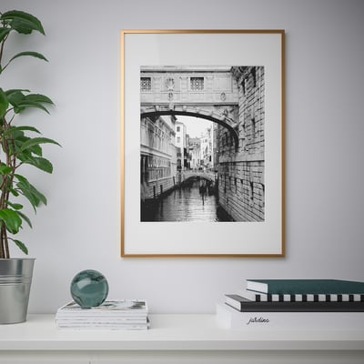 Frame with canal bridge scene, desk, books, plant.