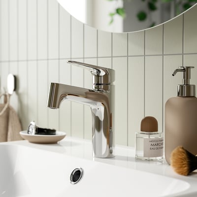 Modern bathroom tap, chrome-plated MAJSJÖN, sleek design, surrounded by toiletries.
