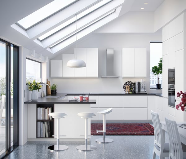 Contemporary white kitchen with modern appliances, white barstools, skylights, and sleek cabinets.