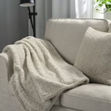 Beige NÄTNÄVA throw & cushion on grey sofa, warm & cosy.