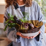 Person holding large glass bowl with dark glaze, red lettuce, and green herbs. Handcrafted, decorative, and modern design.