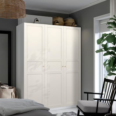 Large white PAX wardrobe beside bed, tall with woven baskets atop, modern design, grey walls.