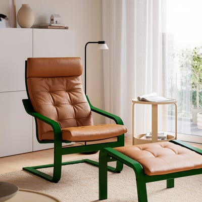 Modern living room with brown leather & green metal armchair & ottoman, white curtains, & small table beside window.