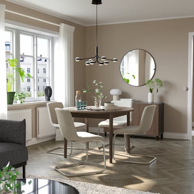 Modern beige dining room with extendable table and metal-trimmed chairs, large mirror, natural light.