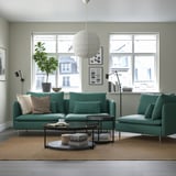 Modern living room with a teal SÖDERHAMN sofa, corduroy texture, armchairs, coffee table, large windows, pendant light, plants, and wall art.