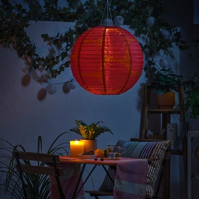 Cosy outdoor dining setup with red lantern, candle, plant, and fruit.