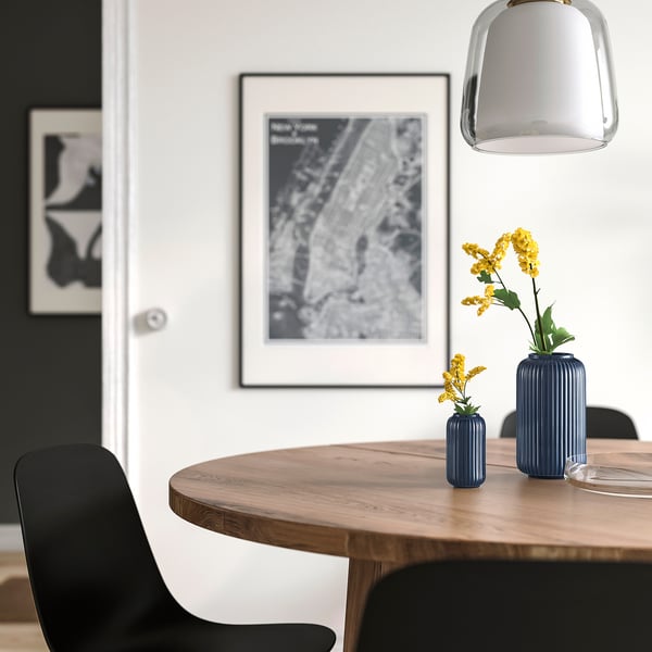 Modern dining set with dark chairs, wooden table, STILREN vases, yellow flowers, abstract art, lighting.