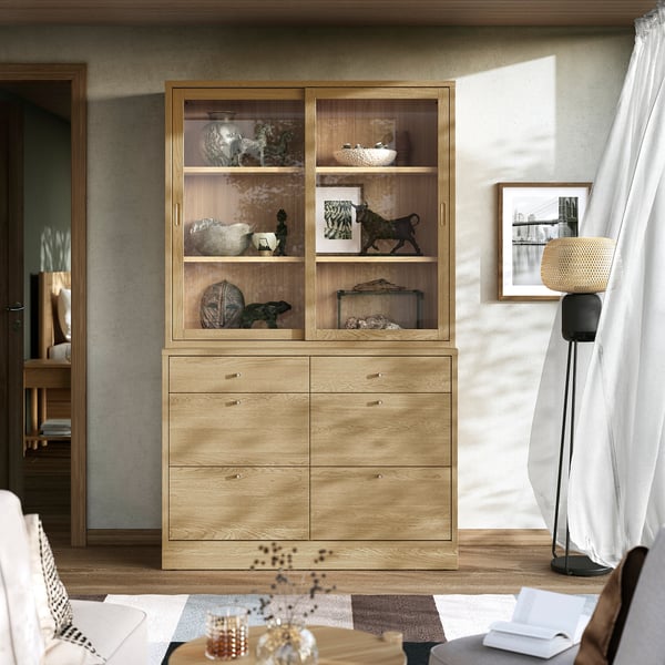 Minimalist wooden cabinet & drawers display art, books. Tall floor lamp beside window. Recliner near coffee table with flowers, remote.