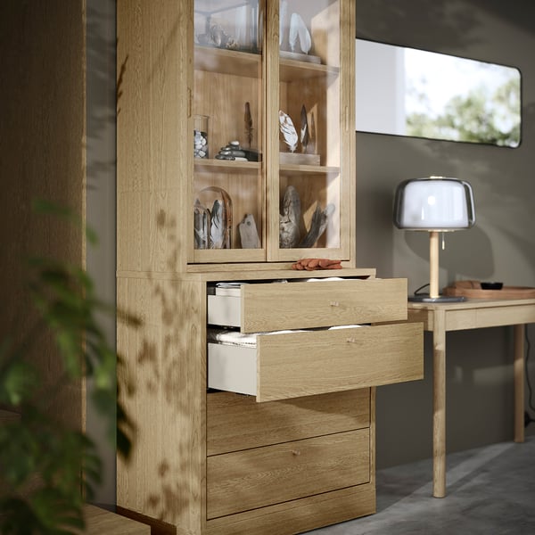 Wooden cabinet with sliding glass doors, displaying decorative items. Below, multiple drawers provide hidden storage.