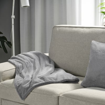 Grey faux fur throw on light sofa, lamp, plant, window.