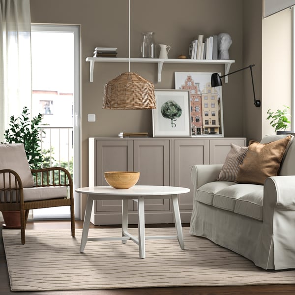A cosy living room with a grey sofa, VÄXELFEL rug, and wooden table, enhanced by a wavy-patterned rug and pendant lamp.