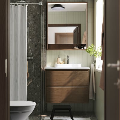 Modern bathroom with brown oak vanity, marble basin, large mirror, and shower curtain. Black stool in front.