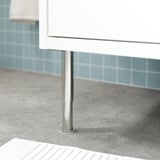 Metal leg stabilizes white bathroom cabinet against blue tiled wall.