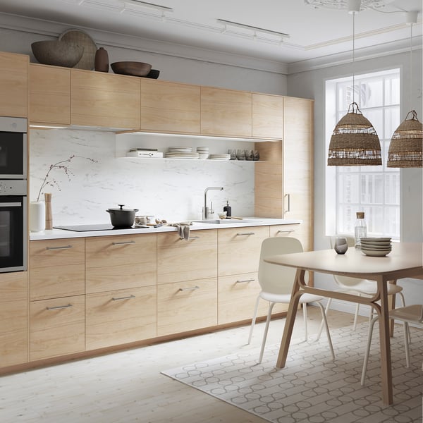 Modern kitchen with light wood cabinets, marble countertops, and rattan pendant lights.