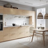 Modern kitchen with light wood cabinets, marble countertops, and rattan pendant lights.