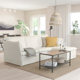 White BACKSÄLEN sofa with chaise, yellow/gray pillows, wooden coffee table, modern lamp, large window.