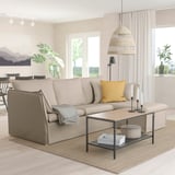 Modern living room with beige BACKSÄLEN sofa, yellow pillow, wooden coffee table, black candlesticks, large window, natural light, cozy decor.