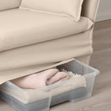 A beige sofa with a clear storage container underneath, holding folded blankets.