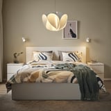 Bedroom with large pendant lamp over patterned bed, flanked by nightstands, beige walls.
