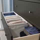 Organized drawer with BAXNA fabric organizers in blue and beige, neatly storing t-shirts and towels in a grey dresser.