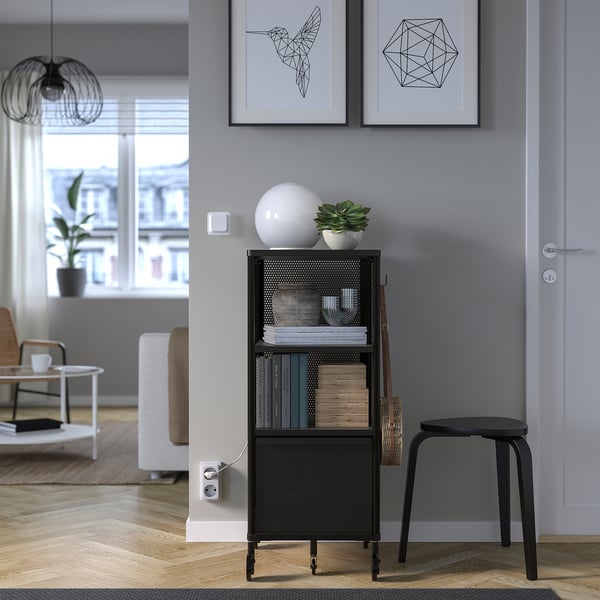 Modern living room with bookshelf, books, decor, plant. Framed art, door, stool, couch, coffee table, lamp.