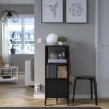 Modern living room with bookshelf, books, decor, plant. Framed art, door, stool, couch, coffee table, lamp.