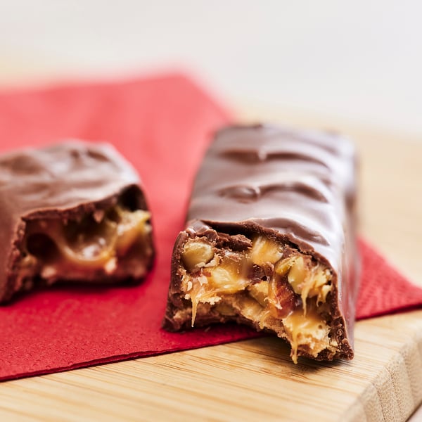Two chocolate bars with bite marks, revealing chewy caramel and nutty filling, placed on a red napkin.