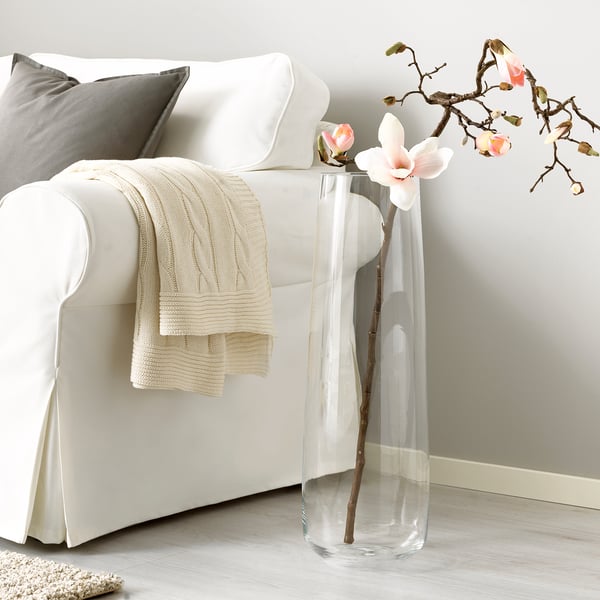 BERÄKNA glass vase with flowers beside sofa.