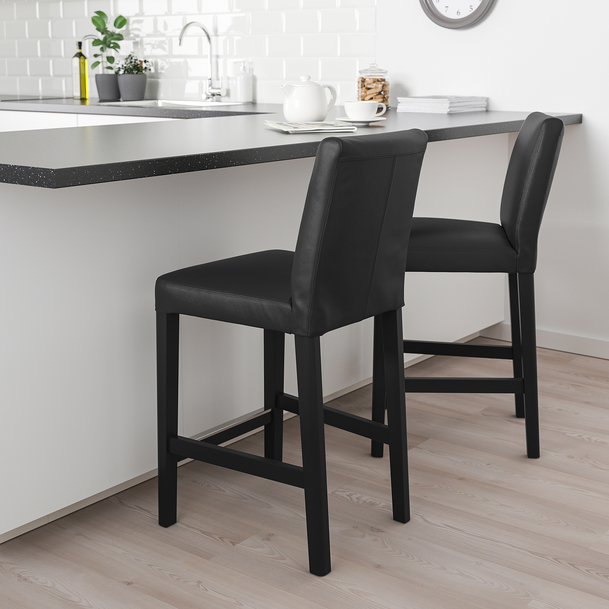 Modern black leather stools at kitchen island with teapot, cups, and plant.